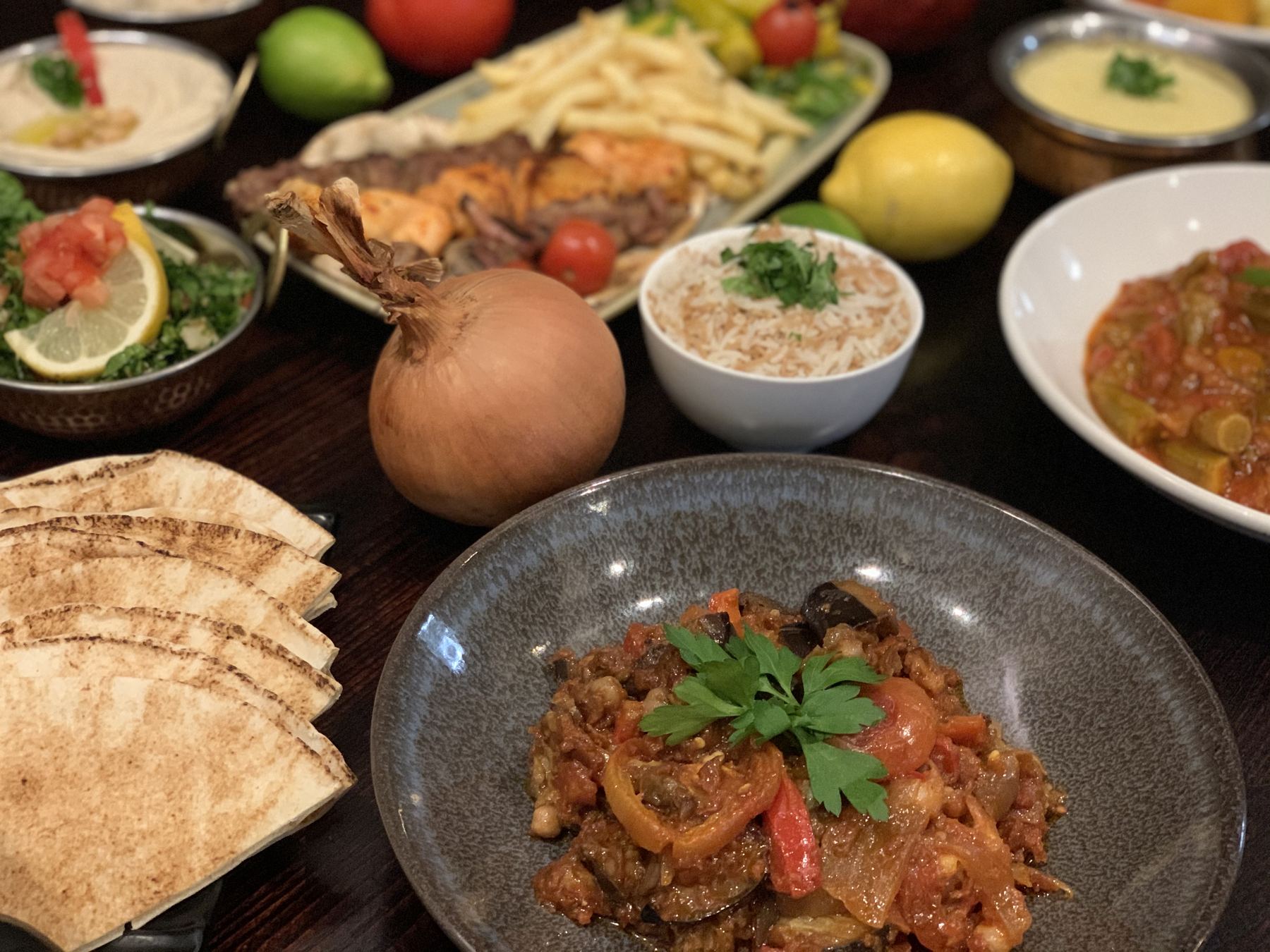 A table laid with okra stew, mixed grill, rice, dips and Lebanese bread